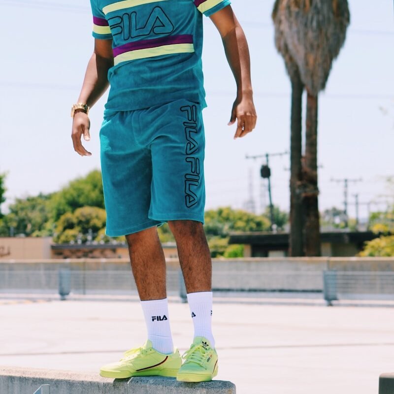 man in teal Fila T-shirt and shirts standing near palm tree in park